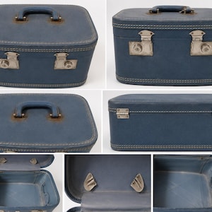 May include: A blue hard-shell train case with a top handle, silver-toned metal latches, and a lock mechanism. The exterior features stitched detailing along the edges. The interior is lined in blue and includes two small side pockets for storage.