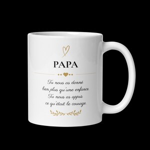 Peut inclure: Un mug en céramique blanc orné d'un cœur doré au-dessus du mot PAPA en noir. En dessous, une ligne horizontale dorée avec un cœur et le texte : Tu nous as donné bien plus qu'une enfance. Tu nous as appris ce qu'était le courage.