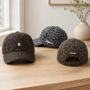Può includere: Tre cappellini da baseball con stampa leopardata. Un cappellino marrone presenta la lettera bianca R. Un cappellino grigio presenta la scritta bianca Weiyaman. Un cappellino marrone presenta la scritta bianca Classic e un cinturino regolabile.
