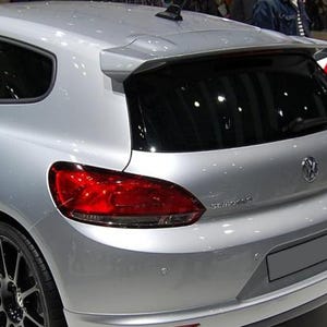 Puede incluir: Un Volkswagen Scirocco plateado tipo hatchback visto desde el ángulo trasero de tres cuartos. El vehículo cuenta con un alerón de techo prominente, ventanas traseras tintadas oscuras, luces traseras rojas, un emblema central de Volkswagen y llantas negras.