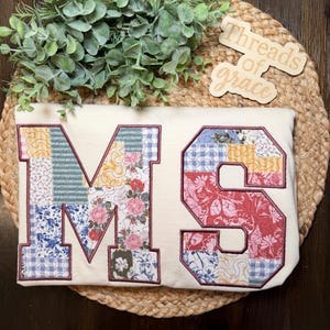 May include: A cream-colored sweatshirt featuring large, block-style letters M and S. The letters are filled with a patchwork design of various floral and gingham patterns in shades of blue, red, yellow, and green, outlined in a dark maroon thread.