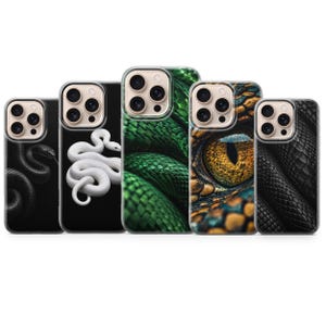 Peut inclure: Cinq coques de smartphone alignées, chacune présentant un motif unique sur le thème du serpent. Les designs incluent un serpent noir sur fond noir, un serpent blanc sur fond noir, des écailles vertes, un œil de reptile et des écailles noires.
