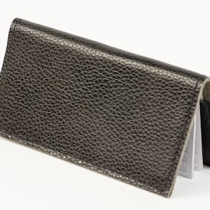 May include: A black leather card holder with a textured finish. The holder is folded closed and has a white interior.