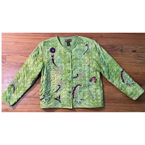 May include: A light green long-sleeve jacket with a textured, woven-look fabric. The jacket features a round neckline, a front button closure, and decorative embroidery in shades of purple, teal, and yellow, depicting floral and abstract shapes.