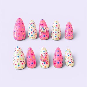 May include: A set of ten almond-shaped press-on nails featuring a vibrant polka dot pattern in shades of pink, blue, yellow, and orange. Some nails have a bright pink base, while others have a cream base. Two nails feature a small 3D dog charm.