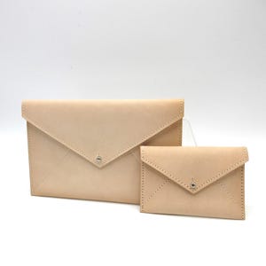 May include: Two natural-colored leather envelope-style pouches. The larger pouch has a flap closure with a silver snap. The smaller pouch also has a flap closure with a silver snap. Both pouches have stitched detailing.