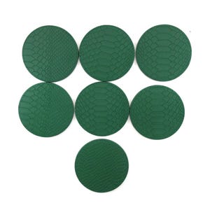 May include: Seven circular, emerald green coasters with a textured, snakeskin-like pattern. The coasters are arranged on a white background. The coasters are made of a durable material and are designed to protect surfaces from spills and condensation.