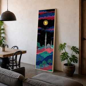 May include: A tall, rectangular framed wall art piece featuring a pointillist landscape at night. The scene depicts a mosque with a minaret under a dark sky with a glowing yellow moon, pink and blue clouds, and rolling hills in shades of blue and red.