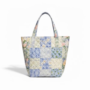 May include: A quilted tote bag featuring a patchwork design of various floral and botanical patterns in shades of light blue, cream, and soft pink. The bag has two matching fabric handles and a structured rectangular shape with diamond stitching.