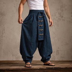 Puede incluir: Pantalones de color azul profundo con corte holgado, diseño de cintura alta cruzada y un panel vertical central. El panel está asegurado por cinco cierres de tela horizontales con nudos. Los pantalones tienen una silueta ancha y lazo en la cintura.