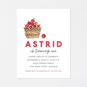 May include: A red and white watercolor illustration of a basket full of red apples. The text "Astrid is turning one" is below the basket. The invitation includes the date, time, location, and RSVP information.