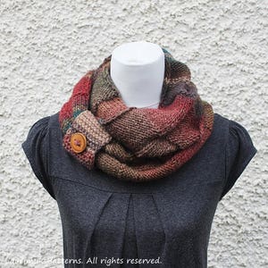 May include: A knitted infinity scarf with a brown button closure. The scarf is made in a variety of colors, including red, brown, green, and blue.