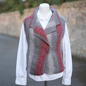 May include: A gray and red knitted vest with a wide collar. The vest is sleeveless and has a slightly asymmetrical design.