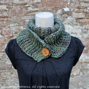 May include: A green, purple, and brown knitted cowl with a wooden button. The cowl is worn on a gray shirt.
