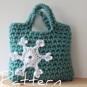 May include: A teal crocheted tote bag with a white crocheted snowflake design. The bag has two handles and is sitting on a wooden surface.