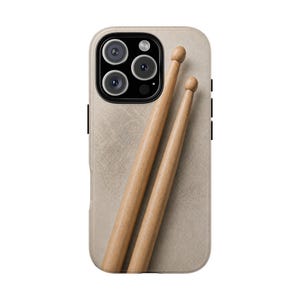 May include: A smartphone case featuring a textured, light beige background with a graphic print of two wooden drumsticks placed diagonally across the center. The case has a cutout for a triple-lens camera system on the upper left side.