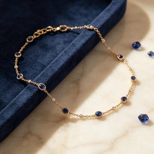 May include: A gold chain bracelet featuring alternating round blue sapphire gemstones and small clear white diamonds set in individual bezels. The delicate link chain includes a lobster clasp and a short extender chain with small circular links.
