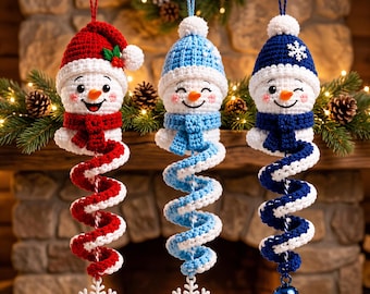 May include: Three crocheted snowman ornaments hanging vertically. The left snowman wears a red hat with holly, the center a light blue hat, and the right a dark blue hat with a snowflake. Each has a spiral body and a white snowflake or bell.