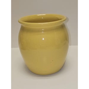 May include: A solid yellow ceramic crock with a smooth, glossy finish and a wide, rounded body. The vessel features a thick, rolled rim at the top opening and a slightly tapered base, presenting a simple, functional design with no additional patterns.
