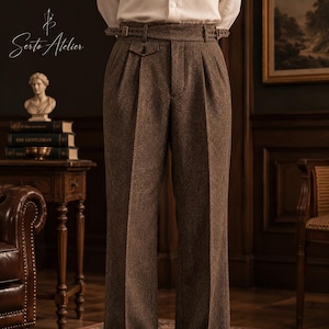 Può includere: Pantaloni marroni a vita alta con un sottile motivo a spina di pesce, doppie pieghe sul davanti e una cintura con fibbia regolabile in vita. I pantaloni hanno un taglio a gamba dritta e sono abbinati a una camicia bianca e scarpe scure.