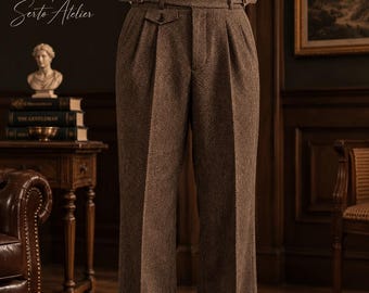 May include: High-waisted brown trousers featuring a subtle herringbone pattern, double pleats at the front, and a buckled side-adjuster belt at the waist. The trousers have a straight-leg cut and are paired with a white shirt and dark shoes.