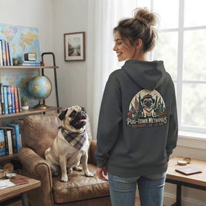 May include: A dark gray hooded sweatshirt featuring a graphic on the back of a pug wearing a hat and scarf, with the text PUG-TOWN METROPOLIS EXPLORER'S CLUB EST 1984, set against a stylized city skyline illustration in muted colors.
