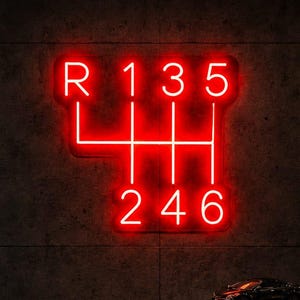 May include: A bright red neon sign mounted on a dark concrete wall, displaying a manual transmission gear shift pattern with the letters R, 1, 3, 5 on the top row and 2, 4, 6 on the bottom row, connected by straight glowing red lines.