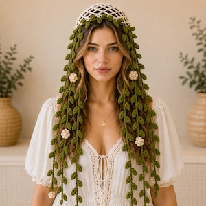 May include: A crochet headpiece featuring an off-white lattice cap adorned with long, cascading green vine strands. The vines are decorated with small, crocheted off-white flower blossoms interspersed throughout the length of the foliage.