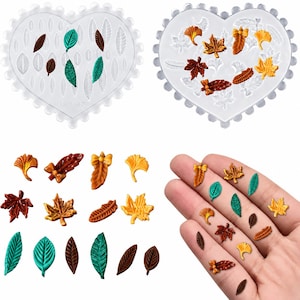 May include: Two heart-shaped silicone molds with various leaf-shaped cavities, accompanied by a collection of small, colorful resin leaf embellishments in shades of brown, orange, yellow, and green, including maple, ginkgo, and elongated leaf shapes.