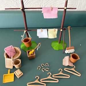 May include: A miniature laundry set featuring a brown plastic clothesline with hanging pink, white, and yellow fabric cloths. Accessories include brown buckets, a mop, a washboard, a yellow dustpan, a soap bar, five plastic hangers, and small hooks.