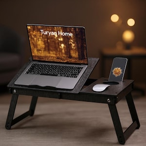 May include: A dark wood laptop desk with foldable legs, featuring an angled platform for a laptop displaying the text Turyan Home, a side section with a circular cutout for a drink, a slot for a smartphone, and a white computer mouse.