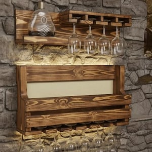 May include: A wall-mounted wooden wine rack system featuring two tiers of dark stained wood with visible grain. The top shelf holds a glass decanter and four hanging wine glasses. The bottom shelf provides additional storage with space for more glasses.