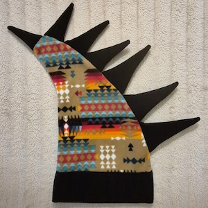 May include: A fleece hat featuring a solid black base and a wide band, with a tall, curved crest adorned with a multi-colored geometric pattern in shades of tan, orange, red, blue, and white, topped with six pointed black fabric spikes.