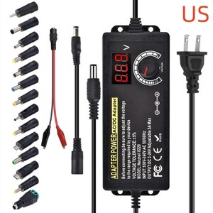 May include: A black AC/DC power adapter featuring a digital voltage display and a rotary dial for adjustment. It includes a US-style power plug, a main cable, and a set of fourteen interchangeable connector tips and cables for various electronic devices.