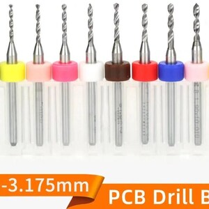 May include: A set of ten metal PCB drill bits with colored plastic rings, arranged in individual clear protective cases. The text 0.1-3.175mm PCB Drill Bit is displayed at the bottom. Each drill bit features a silver shank and a spiral cutting tip.