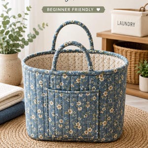 Pode incluir: Um molde de costura para saco de lavandaria azul acolchoado com estampado floral, duas pegas almofadadas e um bolso frontal. O texto diz LAUNDRY BUCKET BAG sewing pattern, BEGINNER FRIENDLY, A0 A4 US LETTER, 2 SIZES REGULAR & LARGE, FRONT POCKET FOR STORAGE, QUILTED & STRUCTURED, PADDED HANDLES.
