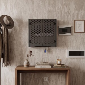 May include: A dark gray wall-mounted cabinet with two doors featuring a diamond-shaped lattice cutout pattern. The cabinet includes a small hook at the bottom center holding a set of keys, providing a functional storage solution for entryways.