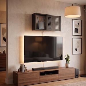 Könnte beinhalten: Ein schwarzer Wandaufbewahrungskasten mit einer schiebbaren Lamellentür, der einen Router enthält, über einem flachen Fernseher mit Hintergrundbeleuchtung, der auf einem langen Holz-Medienboard mit Soundbar und kleiner Pflanze steht.