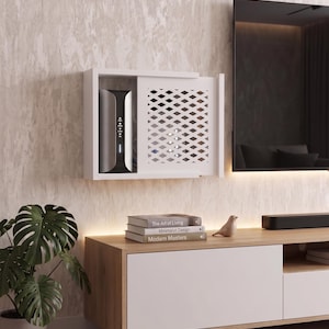 Könnte beinhalten: Eine weiße Wand-Routerbox mit einer Schiebetür im Rautenmuster. Die Box enthält einen schwarz-silbernen Router. Darunter befindet sich ein hölzernes Medienboard mit drei Büchern mit den Titeln The Art of Living, Minimalist Design und Modern Masters sowie einer kleinen Vogelfigur.