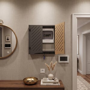 May include: A wall-mounted dark gray cabinet with diagonal slats on the doors, designed to conceal an electrical breaker box. The cabinet features a hinged door that is partially open, revealing the internal panel, and includes hooks for keys.