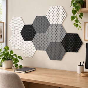 May include: A wall-mounted display consisting of multiple hexagonal pegboards in white, light gray, dark gray, and black. Each board features a uniform grid of vertical slots for organization, arranged in a cluster on a plain wall surface.