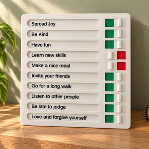 May include: A white plastic task tracker board featuring nine horizontal rows with black text: Spread Joy, Be Kind, Have fun, Learn new skills, Make a nice meal, Invite your friends, Go for a long walk, Listen to other people, Be late to judge, Love and forgive yourself. Each row has a sliding switch with green and red indicators.