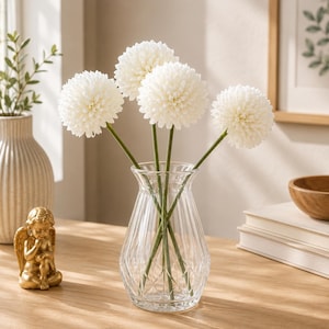 May include: A clear glass vase with a ribbed, diamond-patterned base holds four artificial white globe-shaped flowers on thin green stems. The vase has a flared neck and sits upright, showcasing the stems visible through the transparent glass.