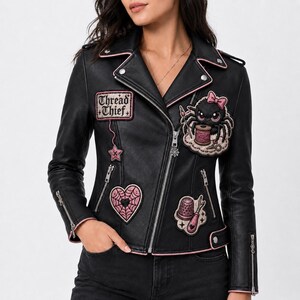 May include: A black faux leather motorcycle jacket featuring pink trim and embroidered patches. The patches include a spider with a spool of thread, a heart-shaped spiderweb, a thimble, a star, and a rectangular patch reading Thread Thief.