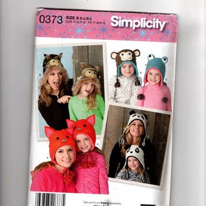 May include: Simplicity pattern featuring various animal-themed hats, including owls, a monkey, a frog, a cat, and a panda. The hats are shown on adults and children. The pattern number is 0373.