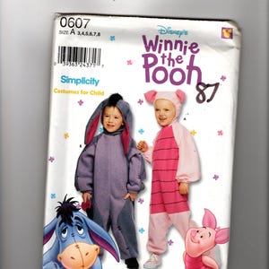 Puede incluir: Un sobre de patrón de costura Simplicity para disfraces infantiles de Winnie the Pooh de Disney, talla A 3,4,5,6,7,8. La portada muestra ilustraciones y fotos de niños con disfraces de Igor y Piglet, con el texto 0607 y 87.