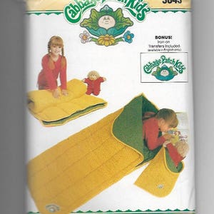 Könnte beinhalten: Ein Vintage-Schnittmuster von Butterick mit Cabbage Patch Kids. Das Muster zeigt einen gelb-grünen Schlafsack mit einem Kind darin. Das Cover enthält das Cabbage Patch Kids-Logo und die Nummer 3045.