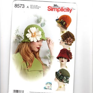 May include: Simplicity pattern 8573 for cloche hats in sizes S-L. The envelope features a green hat with a large white flower, an orange hat, a brown hat with a floral accent, a red hat with a textured trim, and a green patterned hat.