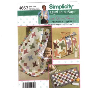 Puede incluir: Patrón Simplicity Quilt in a Day con diseños de edredones de molinillo. El patrón incluye instrucciones para un edredón, una bolsa de pañales y un cambiador. La imagen muestra ejemplos de los productos terminados, como un edredón con un diseño de cruz y una bolsa de pañales de patchwork.