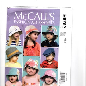 May include: A McCall's Fashion Accessories pattern featuring various children's hats. The hats include a striped hat with a bow, a hat with a coral-colored bow, a plaid bucket hat, a gray hat with a yellow band, a blue newsboy cap, and a pink polka dot hat.